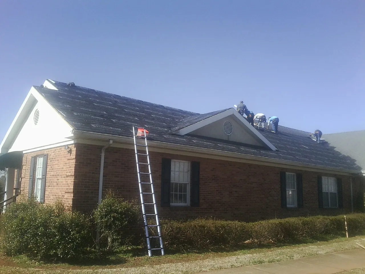 Crew tearing shingles off a brick ranch roof with a ladder set — Metal Roof Repair work by our crew in Pleasant Hill